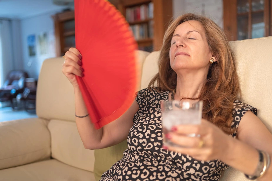 Žena se hladi lepezom i pije vodu zbog valunga, jednog od prvih simptoma menopauze.