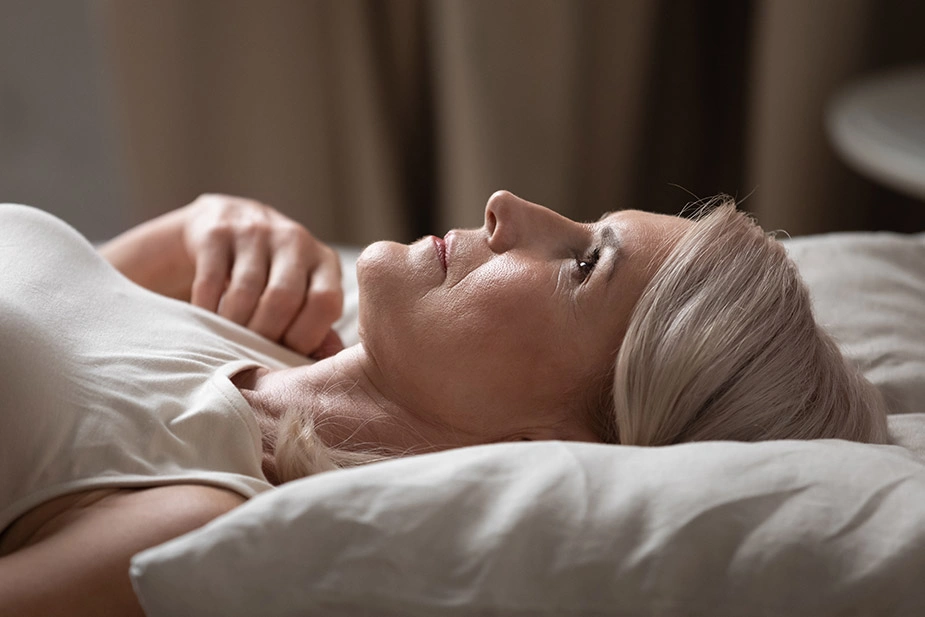 Žena leži budna u krevetu, ne može da zaspi zbog problema sa snom izazvanih prvim simptomima menopauze.