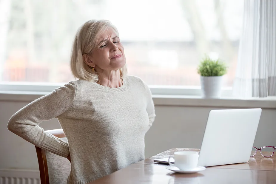 Žena sa bolom u donjem delu leđa sedi za stolom – potencijalni znak problema sa bubrezima u menopauzi.