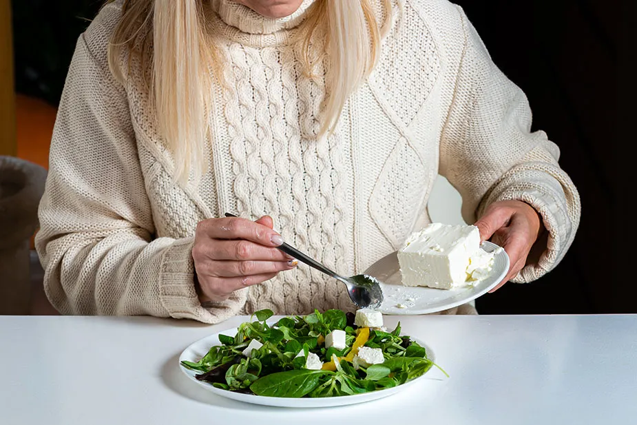 Žena u menopauzi priprema salatu sa sirom i spanaćem