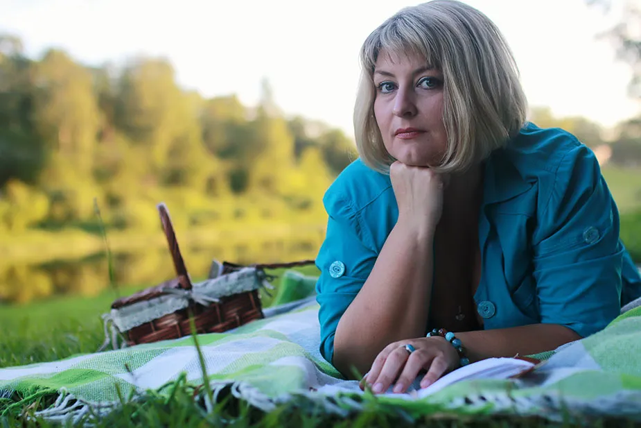 Žena koja se opušta na pokrivaču u prirodi, pored jezera, razmišlja o životu.