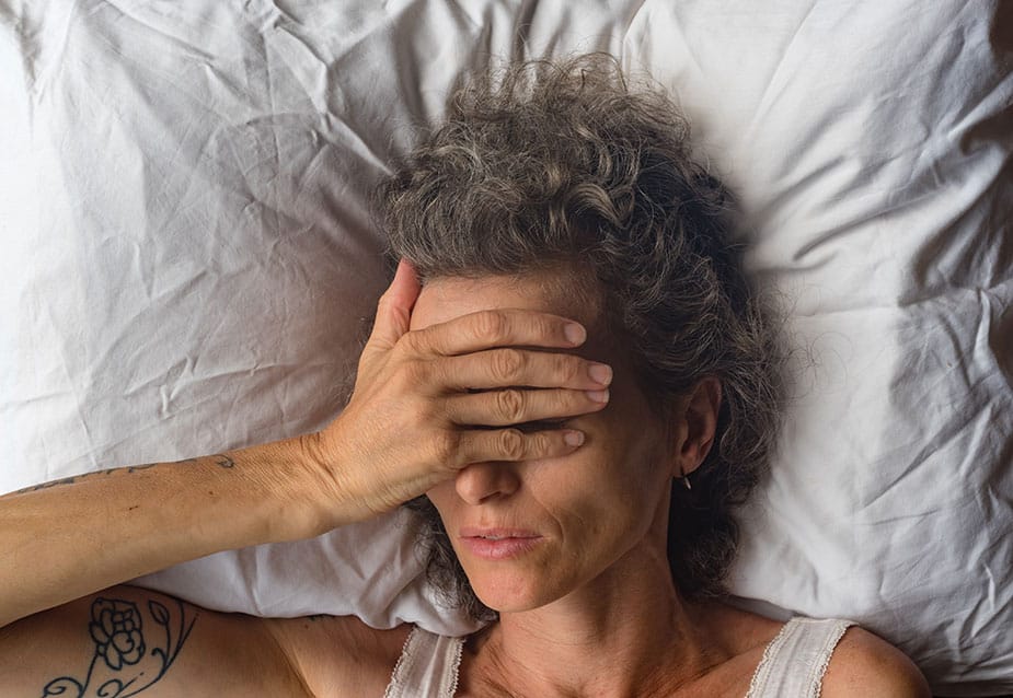 Žena u perimenopauzi leži budna u krevetu sa rukom preko lica — simbol nesanice i valunga.